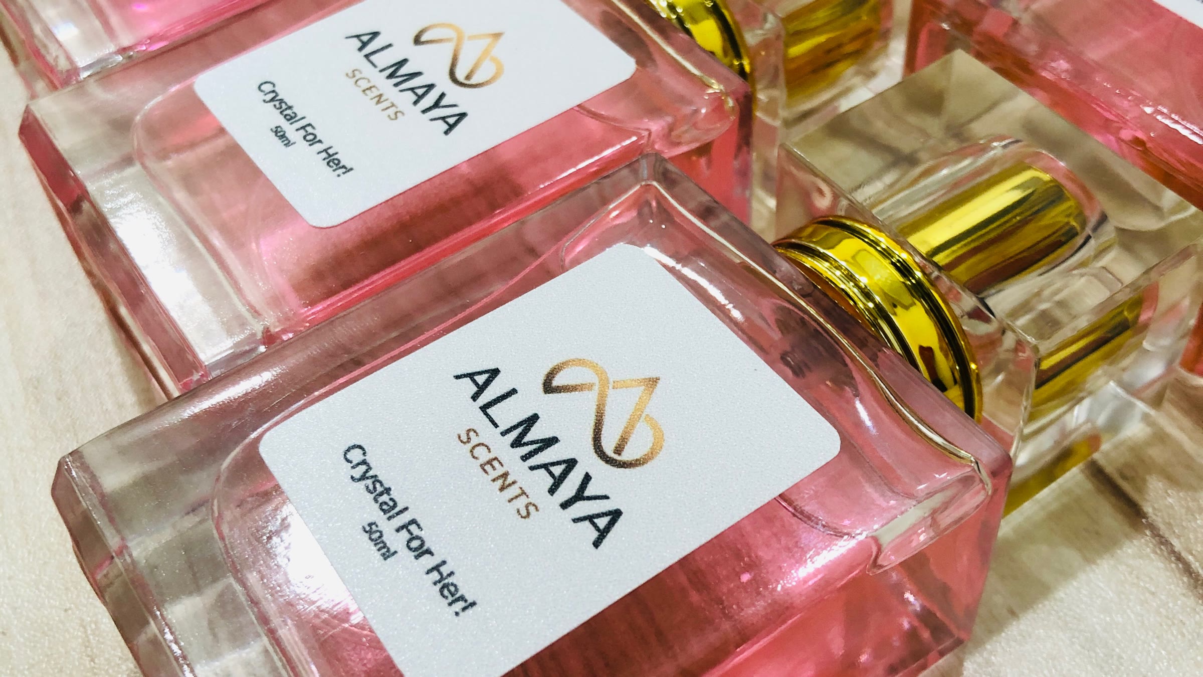Rows of Almaya Scents Crystal For Her bottles on warm wood